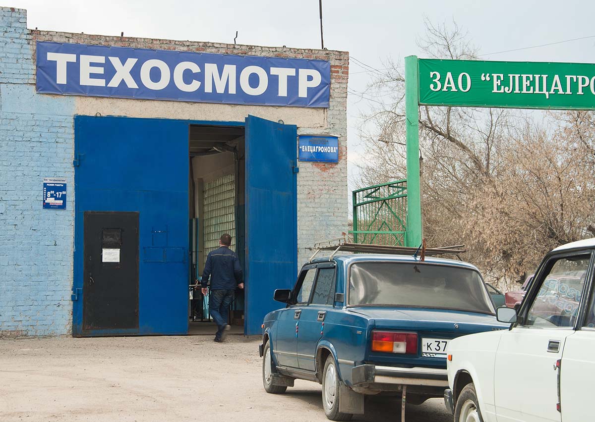 Автовладельцы стоят в очереди на прохождение технического осмотра автомобилей.